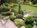 Terraced hillside garden with flagstone patio, wooden footbridge, manicured lawn, and layered ornamental shrubs and perennial plantings
