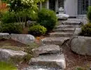 Natural boulder slab pathway with large flat stepping stones leading to front entry flanked by decorative boulders and lush garden beds