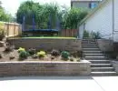 Terraced retaining walls with layered garden beds, ornamental plantings, and concrete staircase alongside two-story home